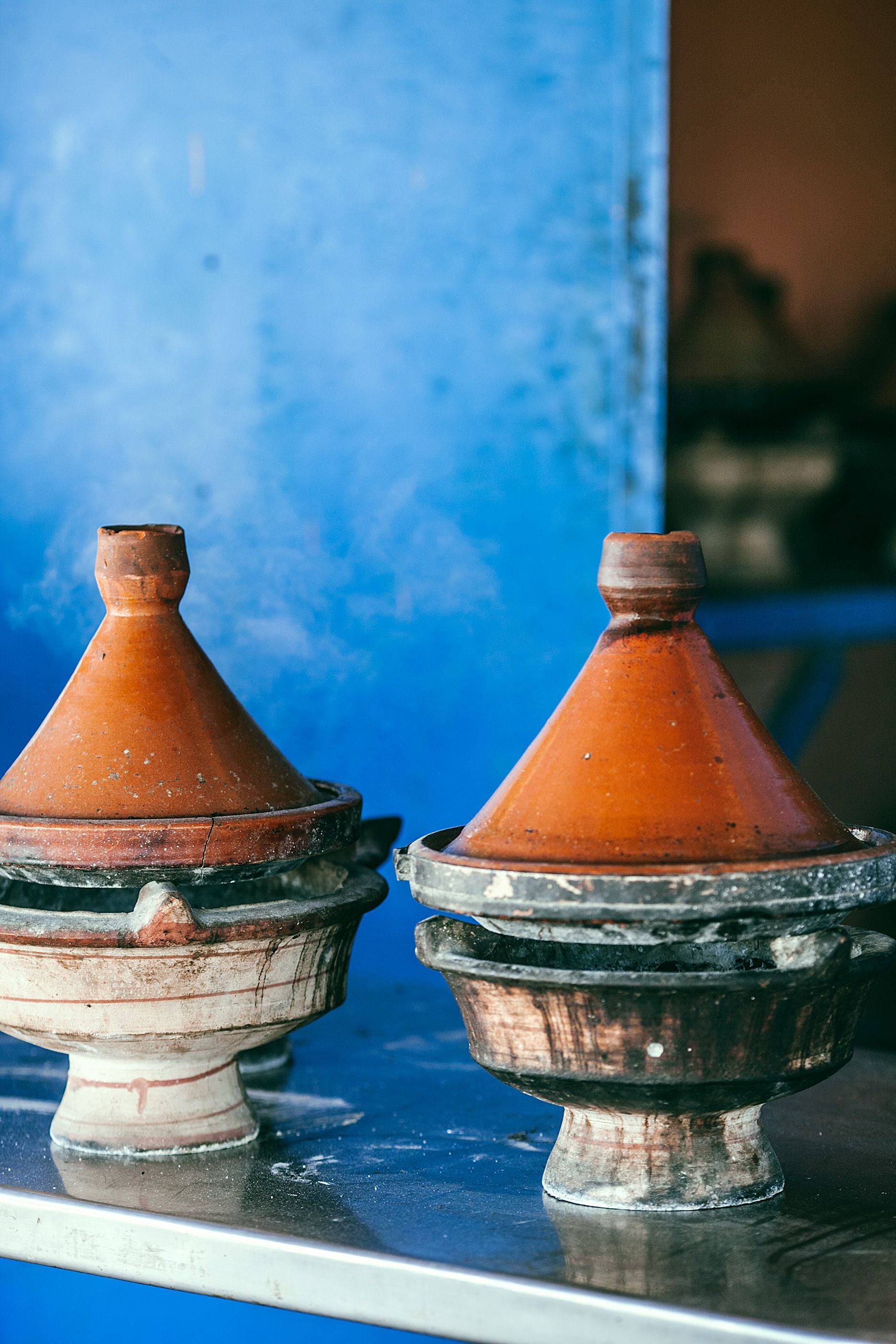 Deux tajines en terre cuite sur une table devant un mur bleu.