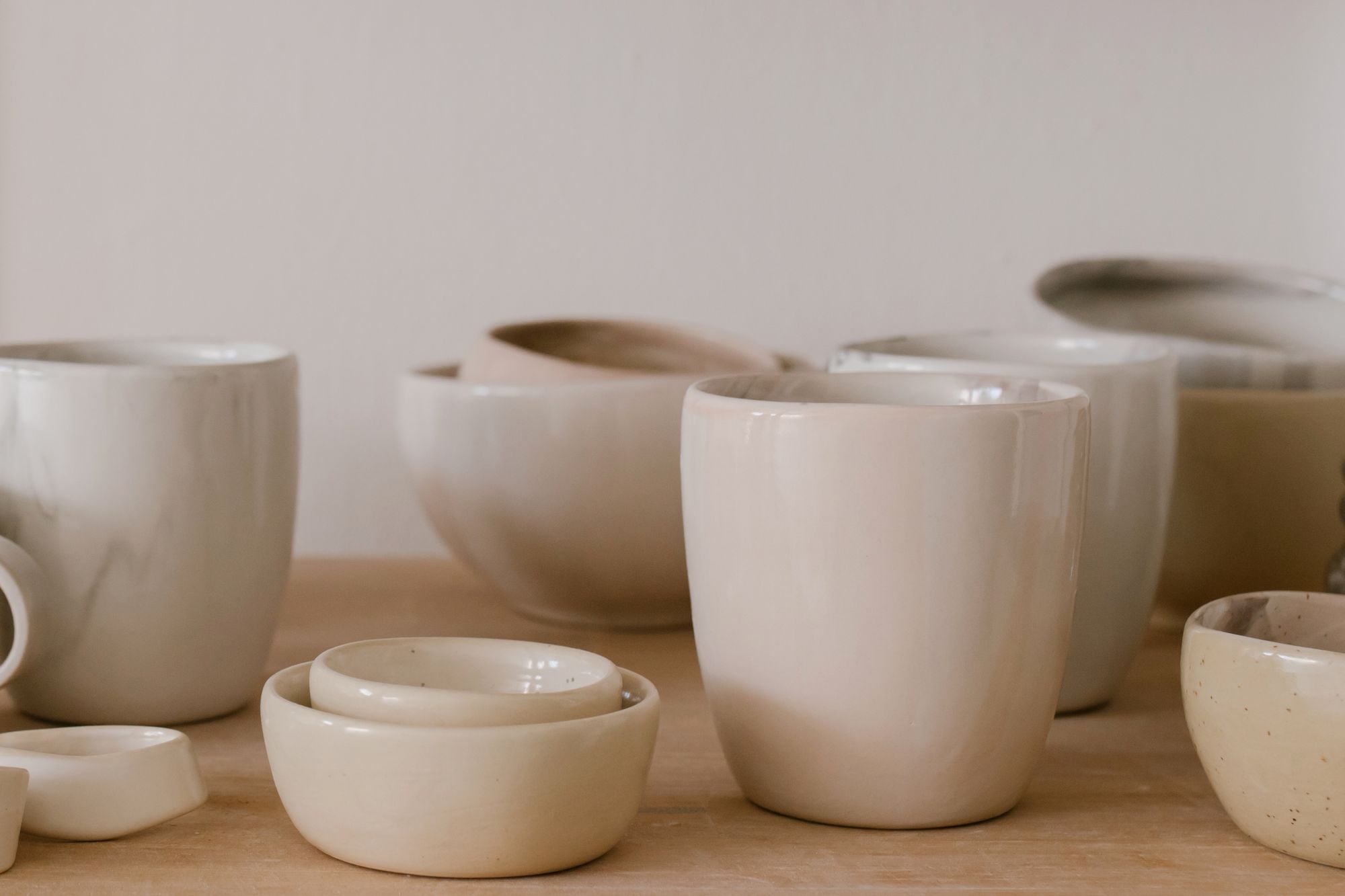 Bols et grandes tasses en céramique claire sur une table en bois.