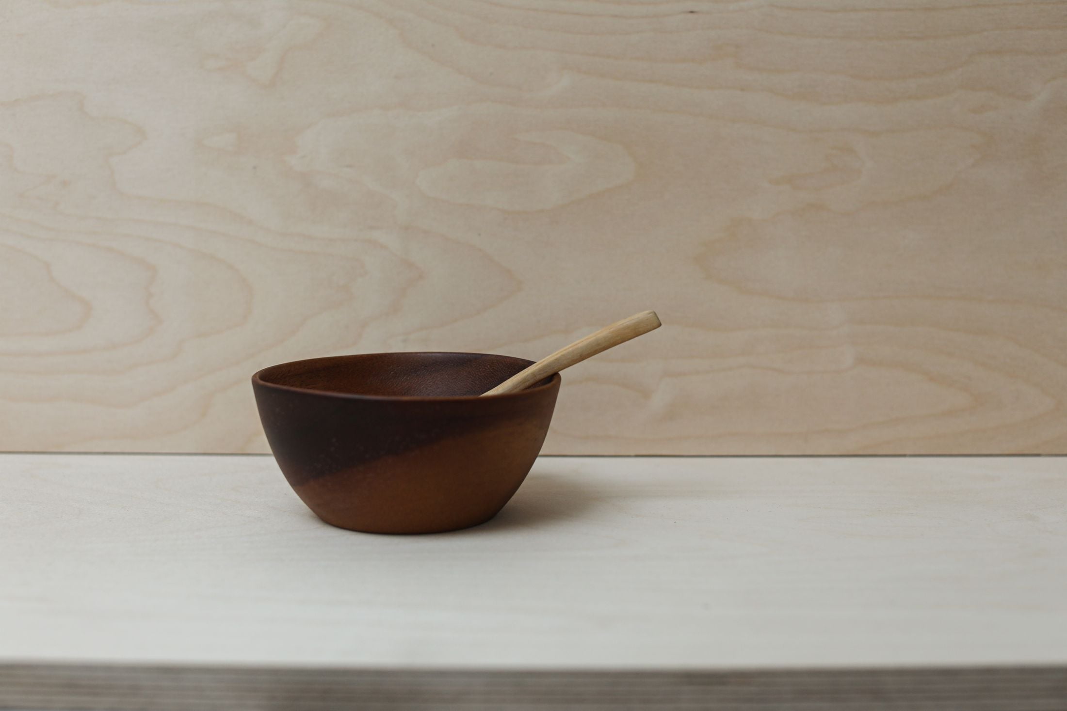Un bol et une cuillère en bois sombre sur une table claire.