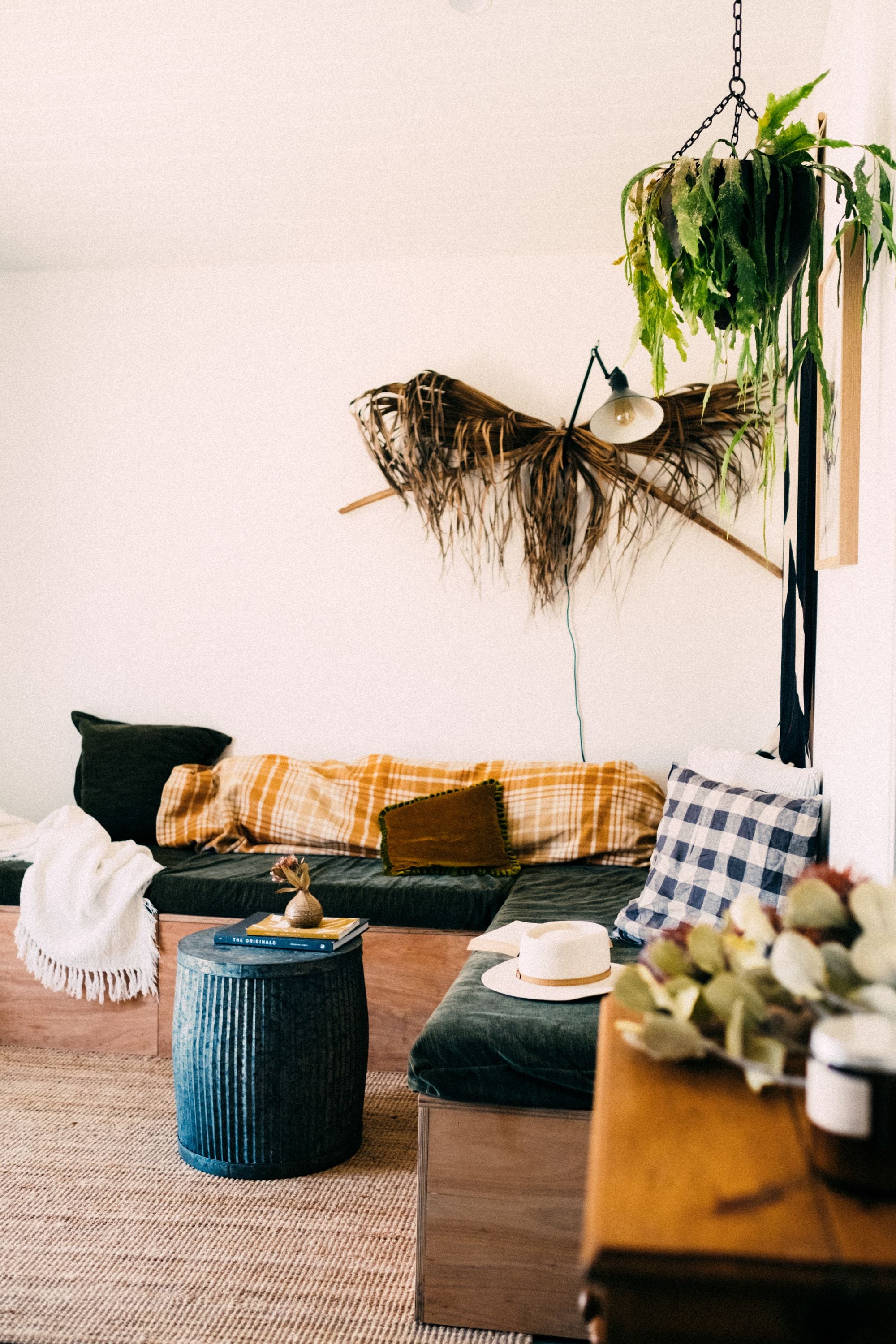 Un salon avec une banquette verte, des coussins ocre et une table en céramique bleue.