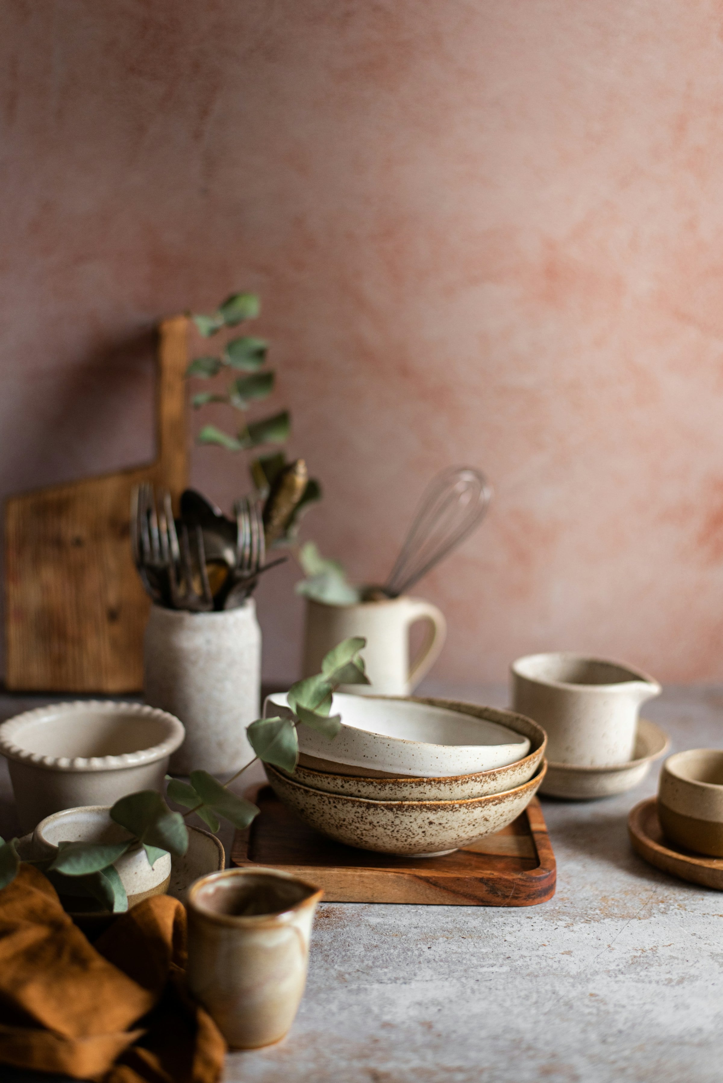 Céramiques, planches en bois et linge ocre devant un mur rose argile.